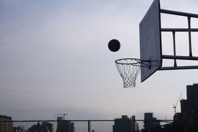 Low angle view of basketball going in hoop against sky during sunset