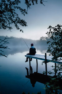 Rear view of woman fishing in lake while sitting on pier