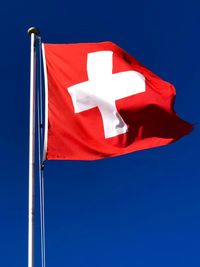 Low angle view of switzerland flag against clear blue sky