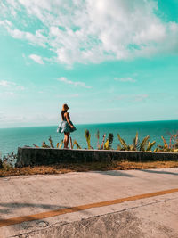 Rear view of woman walking on beach against sky