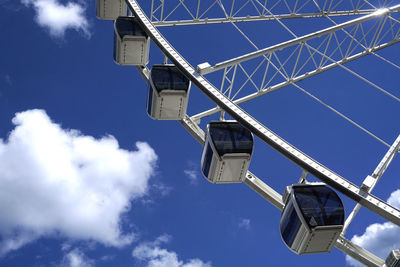 Close-up of a ferris wheel against a blue sky with white clouds