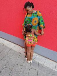 Mother with daughter standing on footpath against wall