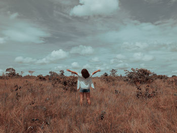 Rear view of woman with arms raised on field against sky