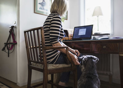 Dog sitting by senior woman using laptop at home