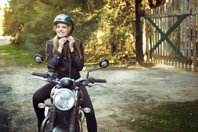 Beautiful woman fastening helmet while sitting on motorcycle