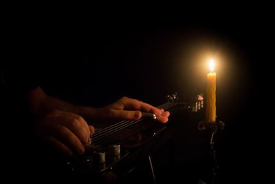 Cropped image of man playing guitar in candlelight at darkroom