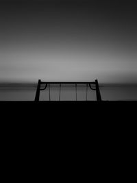 Silhouette railing by sea against sky