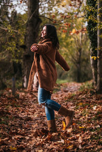 Woman dancing happily on a path covered with dry leaves.