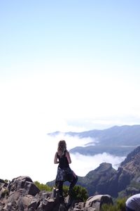 Rear view of woman standing on cliff against sky