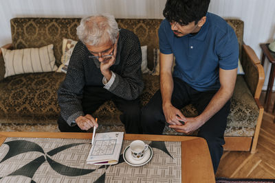 High angle view of senior man playing soduko puzzle while sitting with male caregiver at home