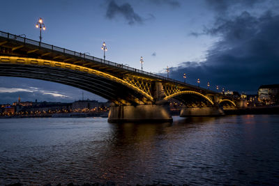 Illuminated bridge over river against sky in city at night