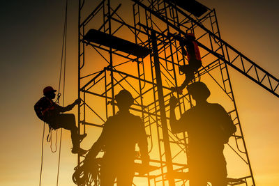 Low angle view of silhouette people working against sky during sunset