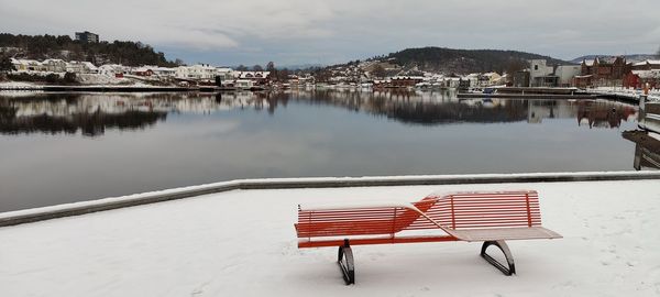 Empty bench by buildings against sky during winter