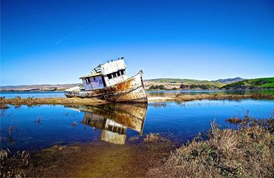 Abandoned boat on calm lake against clear blue sky