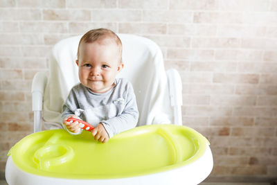 Portrait of cute baby girl sitting on high chair against wall