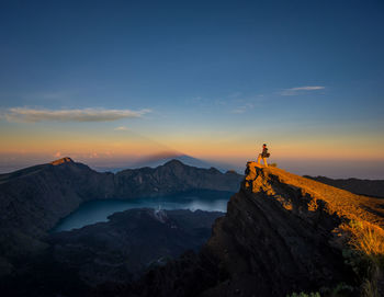 Side view of hiker standing on mountain peak against sky during sunset