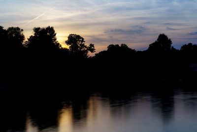 Silhouette trees by lake against sky during sunset