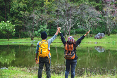 Rear view of couple holding hands while standing by lake at forest