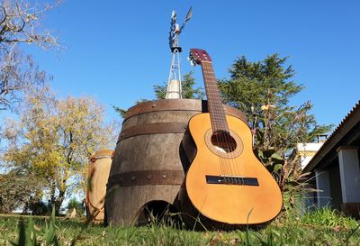 Guitar by tree on field against clear sky