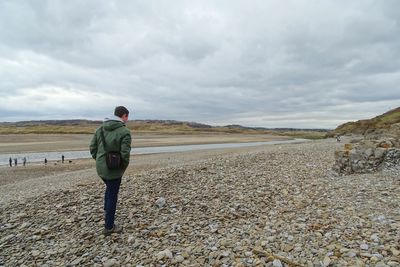 Rear view of man standing on landscape against cloudy sky