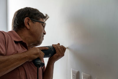 Latino man using a power drill to drill holes in the wall to hang a new television, drilling 