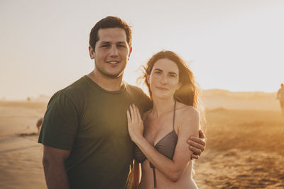 Portrait of smiling couple standing at beach during suset
