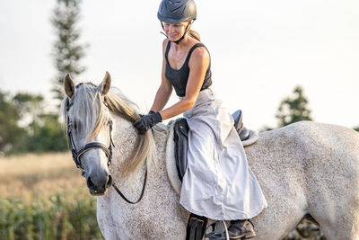 Lusitano horse, white mare, female rider, outdoors on pasture.