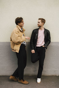 Male friends talking with each other while leaning on beige wall