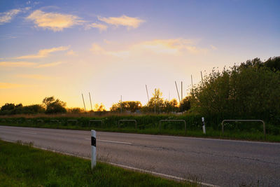 Road by trees on field against sky during sunset