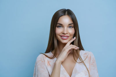 Portrait of beautiful young woman standing against blue background