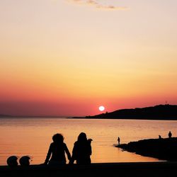 Silhouette people on beach against sky during sunset