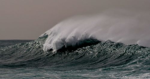 Sea waves splashing on beach against sky