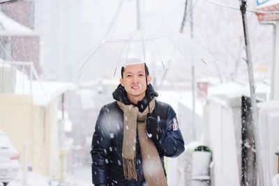 Smiling man holding umbrella during snow fall