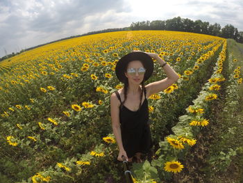 Young woman in a black dress and hat stands on the field with sunflowers in  summer and takes selfie