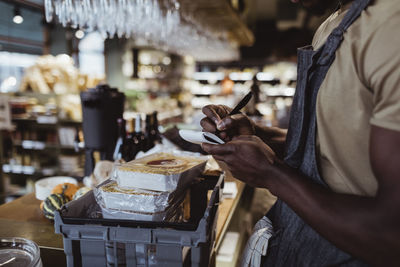 Midsection of male owner writing in note pad at deli store