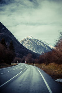 Empty road leading towards mountain against sky during winter