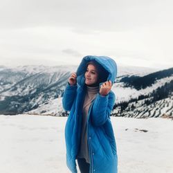 Young woman standing in snow against sky