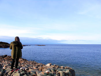 Rear view of woman standing on rock by sea against sky