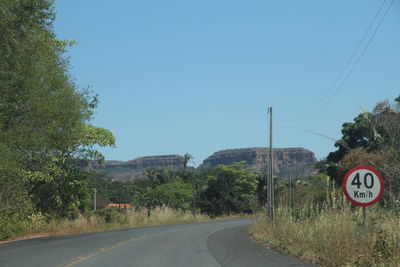 Road sign by trees against clear blue sky