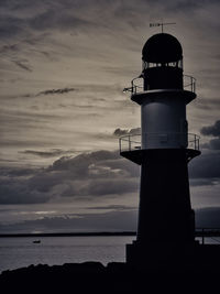 Lighthouse by sea against sky during sunset