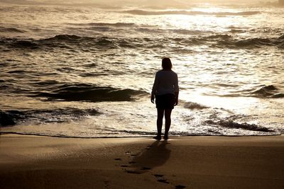 Rear view of woman standing on sand at beach during sunset