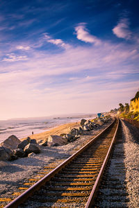 Railroad track by sea against cloudy sky on sunny day