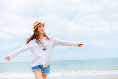 Smiling woman standing at beach against sky