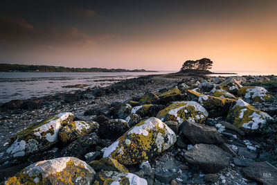 Rocks on beach against sky during sunset