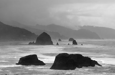 Stack rocks in sea against cloudy sky