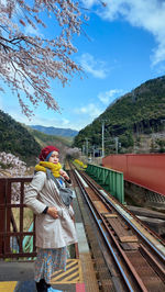 Woman standing by railroad tracks against sky