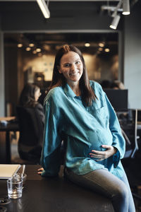 Portrait of pregnant businesswoman sitting at desk in office