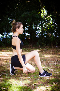 Side view of teenage girl looking away while exercising on field against trees in park