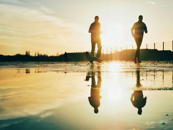Reflection of people in puddle while jogging during sunset