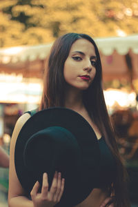 Portrait of a young adult woman loking at camera holding a black hat